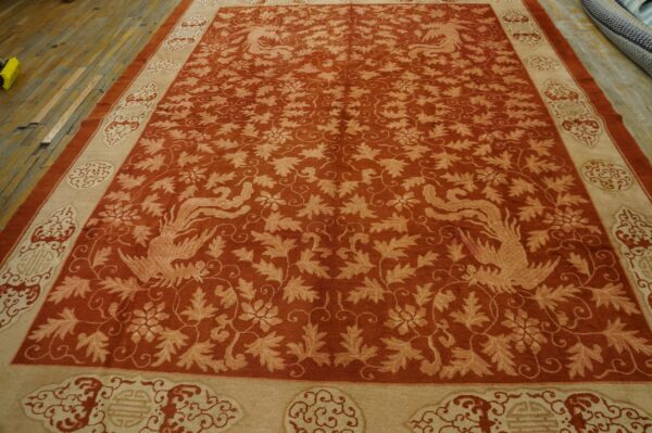 Terracotta rug features a dense botanical pattern, stylized birds, and ornate tan borders on worn wood planks.