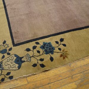 Low-pile mauve and golden rug showing a border design of vines and blue flowers on worn wooden planks.