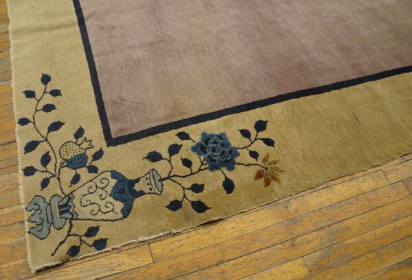 Low-pile mauve and golden rug showing a border design of vines and blue flowers on worn wooden planks.