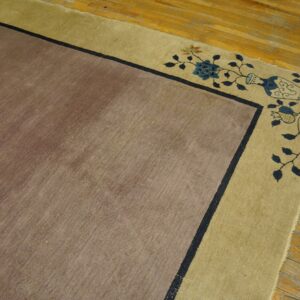 Muted brown rug with dark blue line border and gold edge featuring floral and vase patterns on wood flooring.