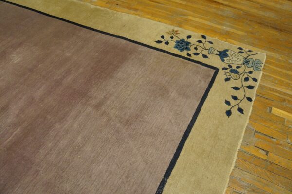 Muted brown rug with dark blue line border and gold edge featuring floral and vase patterns on wood flooring.