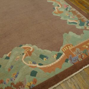 Low-pile taupe rug with a complex pictorial border of green mountains and a terracotta wall on wood flooring.