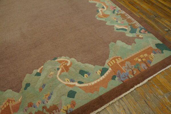 Low-pile taupe rug with a complex pictorial border of green mountains and a terracotta wall on wood flooring.