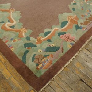 Brown bordered rug with a pastel scenic pattern of green hills, pink blossoms, and camels on distressed wood flooring.