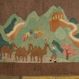 Deep pile rug showing a brown and green landscape with camels and an orange architectural structure over wood floor.
