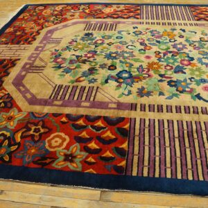 Colorful rug with a beige floral center, multi-colored border panels, and a navy edge on worn wood flooring.