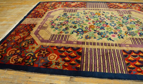 Colorful rug with a beige floral center, multi-colored border panels, and a navy edge on worn wood flooring.