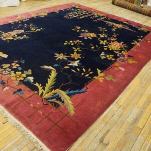 Navy floral rug with a wide pink border lies on a distressed wooden floor in a storage room.