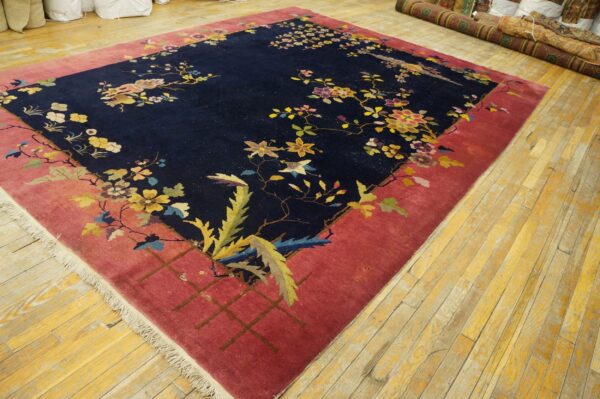 Navy floral rug with a wide pink border lies on a distressed wooden floor in a storage room.