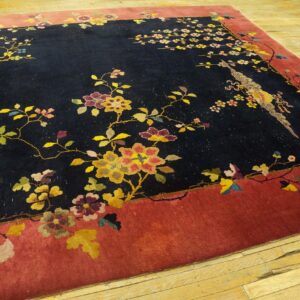A black and red rug with detailed floral and bird designs sits on light wooden floorboards.