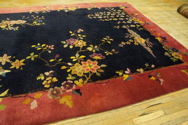 A black and red rug with detailed floral and bird designs sits on light wooden floorboards.