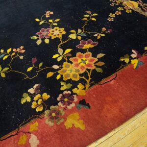 Close-up of a dark blue rug with multicolor floral vines and a rust border on light wood flooring.