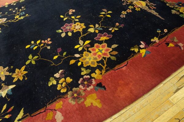 Close-up of a dark blue rug with multicolor floral vines and a rust border on light wood flooring.