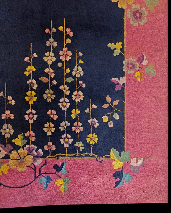 Close-up of a deep navy rug field meeting a bright pink border with multicolored trailing floral patterns.
