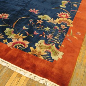 High-pile rug featuring a blue field, colorful floral pattern, and thick rust border on light hardwood flooring.