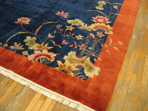 High-pile rug featuring a blue field, colorful floral pattern, and thick rust border on light hardwood flooring.
