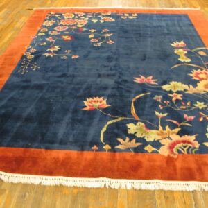 Plush navy rug featuring colorful florals and a wide rust border on light wood floors.