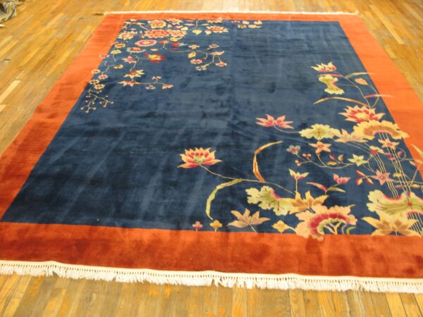 Plush navy rug featuring colorful florals and a wide rust border on light wood floors.