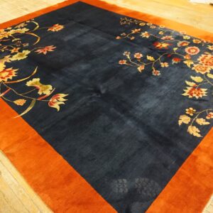 Navy blue rug with vibrant orange border features large red and gold floral motifs on wood flooring.