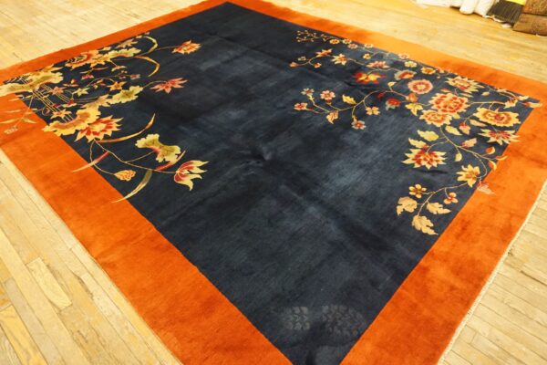 Navy blue rug with vibrant orange border features large red and gold floral motifs on wood flooring.
