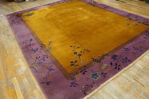 Large gold rug with a wide purple floral border displayed on light worn wood flooring.