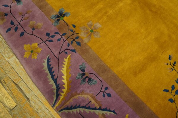 A high-pile rug displays a golden yellow field and a purple floral border next to distressed wood floors.