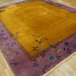 Golden yellow rug with a wide lavender floral border rests on distressed wood plank flooring.