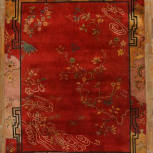 Red rug with scattered floral and cloud designs framed by a geometric gold and black border on wood planks.
