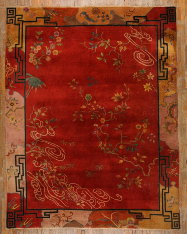 Red rug with scattered floral and cloud designs framed by a geometric gold and black border on wood planks.