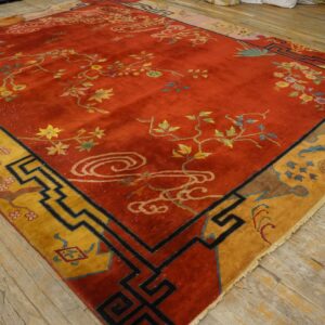 A red rug with low pile features multicolored floral vines and a geometric yellow and black border on wood floors.