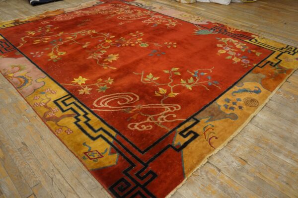 A red rug with low pile features multicolored floral vines and a geometric yellow and black border on wood floors.