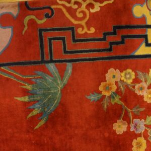 A high-pile red rug with yellow, black, and multicolored floral motifs rests next to worn wooden floorboards.