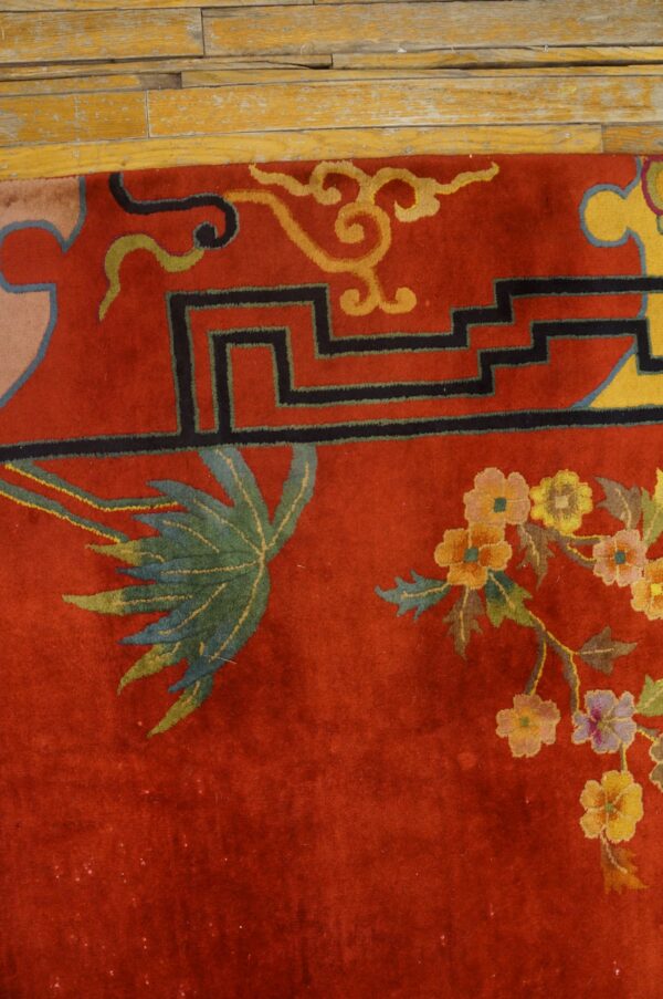 A high-pile red rug with yellow, black, and multicolored floral motifs rests next to worn wooden floorboards.