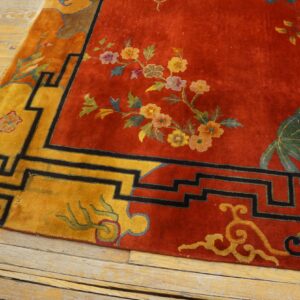 Close-up of a red and gold floral rug featuring a geometric black border on distressed wood floorboards.
