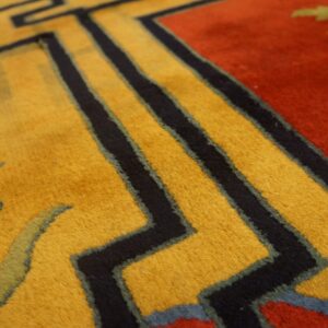 Close-up view of a plush rug featuring gold, red, and black geometric and stylized floral patterns.