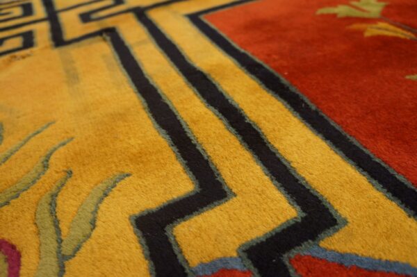 Close-up view of a plush rug featuring gold, red, and black geometric and stylized floral patterns.