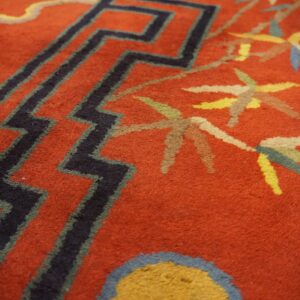 Textured red rug with black chevron patterns and multicolored floral or leaf motifs resting on wood floor.