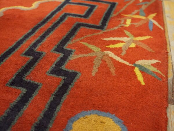 Textured red rug with black chevron patterns and multicolored floral or leaf motifs resting on wood floor.