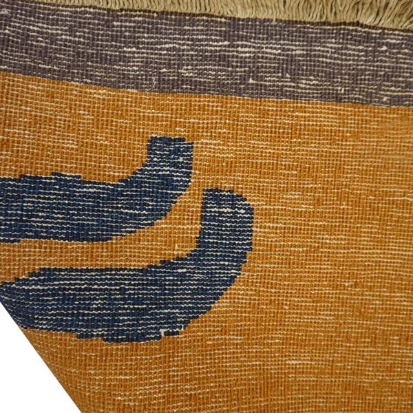 Textured flatweave rug detail in mustard yellow, navy blue, and charcoal gray with tan fringe.