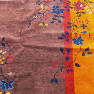 Close-up of a rug featuring a brown field, a yellow border, and a red stripe, decorated with blue florals.