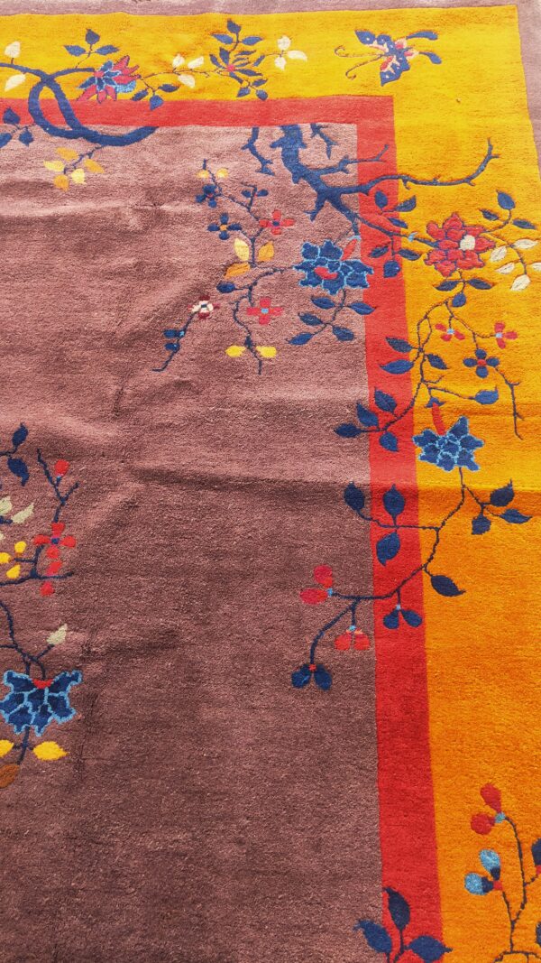 Close-up of a rug featuring a brown field, a yellow border, and a red stripe, decorated with blue florals.