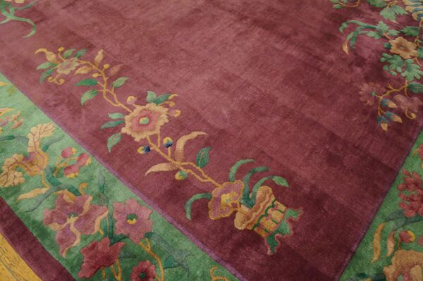 Close-up of a maroon rug field patterned with gold and pink flowers bordering a wide green section.