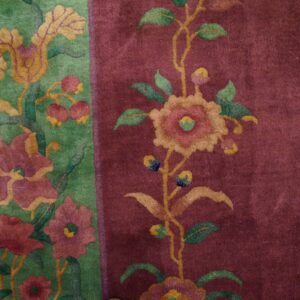 Plush floral rug detail featuring a deep burgundy field and a green border with pink and gold blossoms.