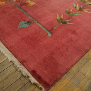 Close-up of a pinkish-red botanical rug with fringe resting on distressed wood planks.