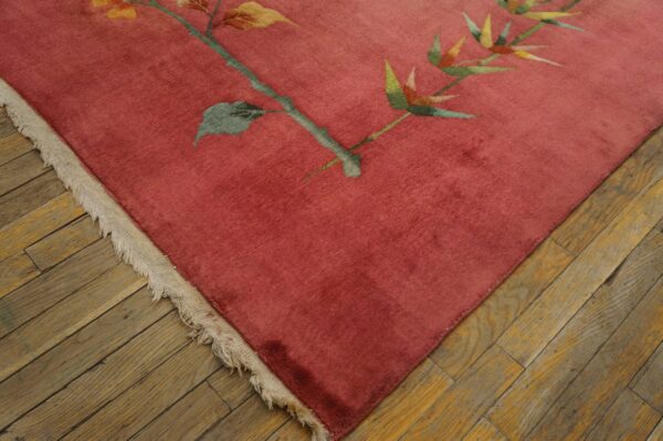 Close-up of a pinkish-red botanical rug with fringe resting on distressed wood planks.