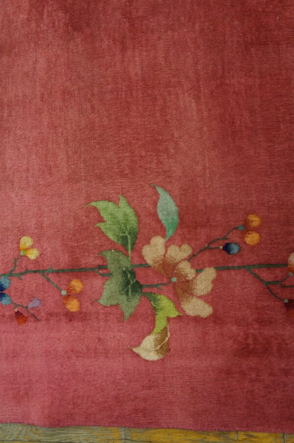 Deep rose plush rug featuring a multicolored floral vine border on distressed wood flooring.