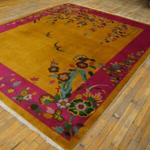 Gold rug with a wide magenta floral border and swallow motifs lies on wood plank flooring.