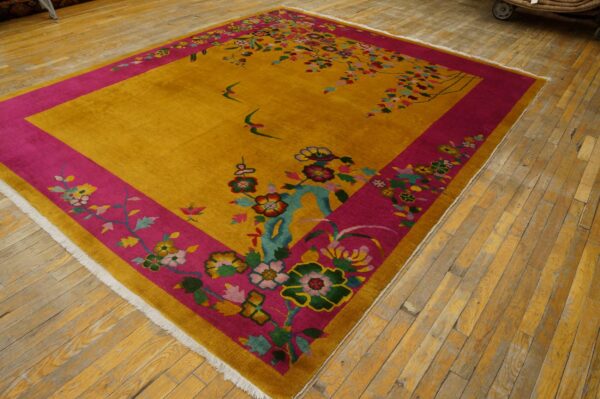 Gold rug with a wide magenta floral border and swallow motifs lies on wood plank flooring.