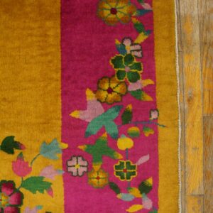 Plush yellow and pink rug with multicolored floral designs, resting on distressed wood planks.