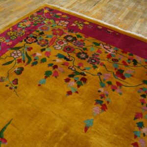 Golden yellow rug with a fuchsia border and multicolored floral pattern resting on distressed wood flooring.